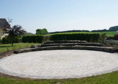 Stor cirkel terrasse med granitsten og beplantning på bagsiden